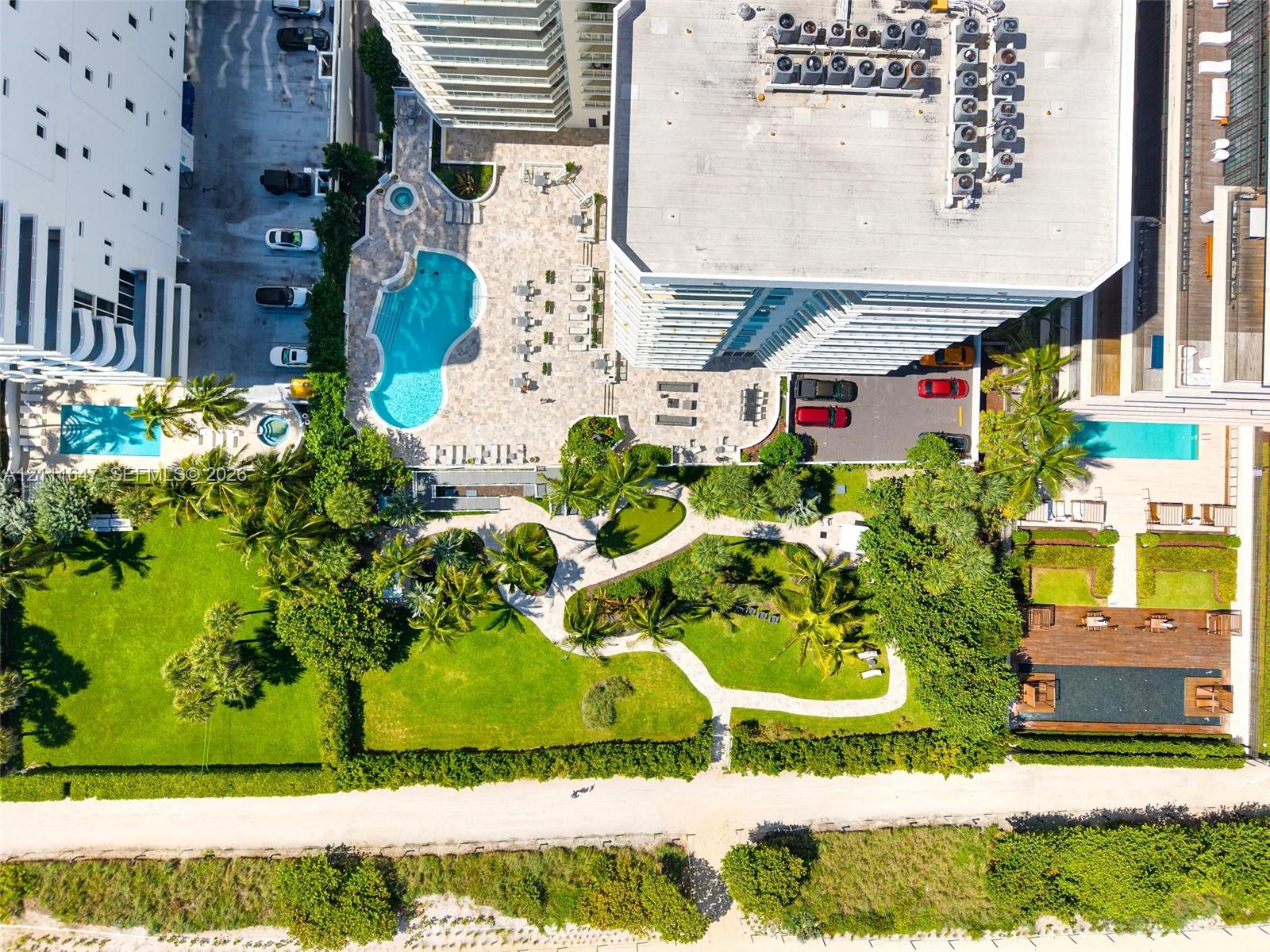 Aerial perspective featuring a swimming pool, integrated spa, expansive landscaped green space with manicured lawn, stone-paved patio, and established palm trees