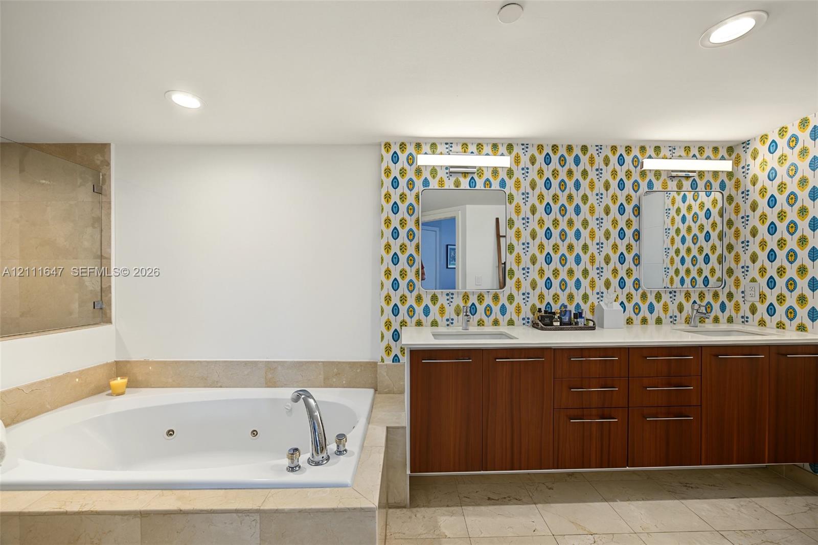 Dual-sink vanity with wood-finish cabinetry, quartz countertops, jetted soaking tub, stone tile surround, and recessed lighting