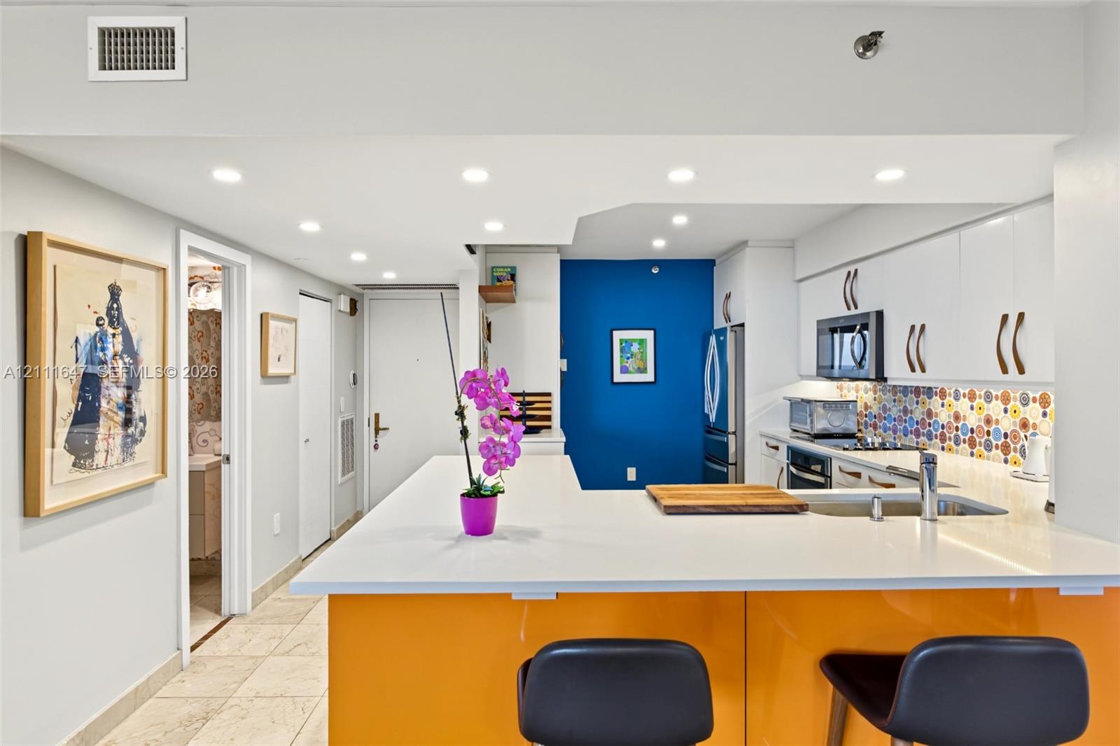 Kitchen featuring a peninsula with quartz countertop, white cabinetry, white upper cabinets, stainless steel appliances, and a multicolor patterned backsplash