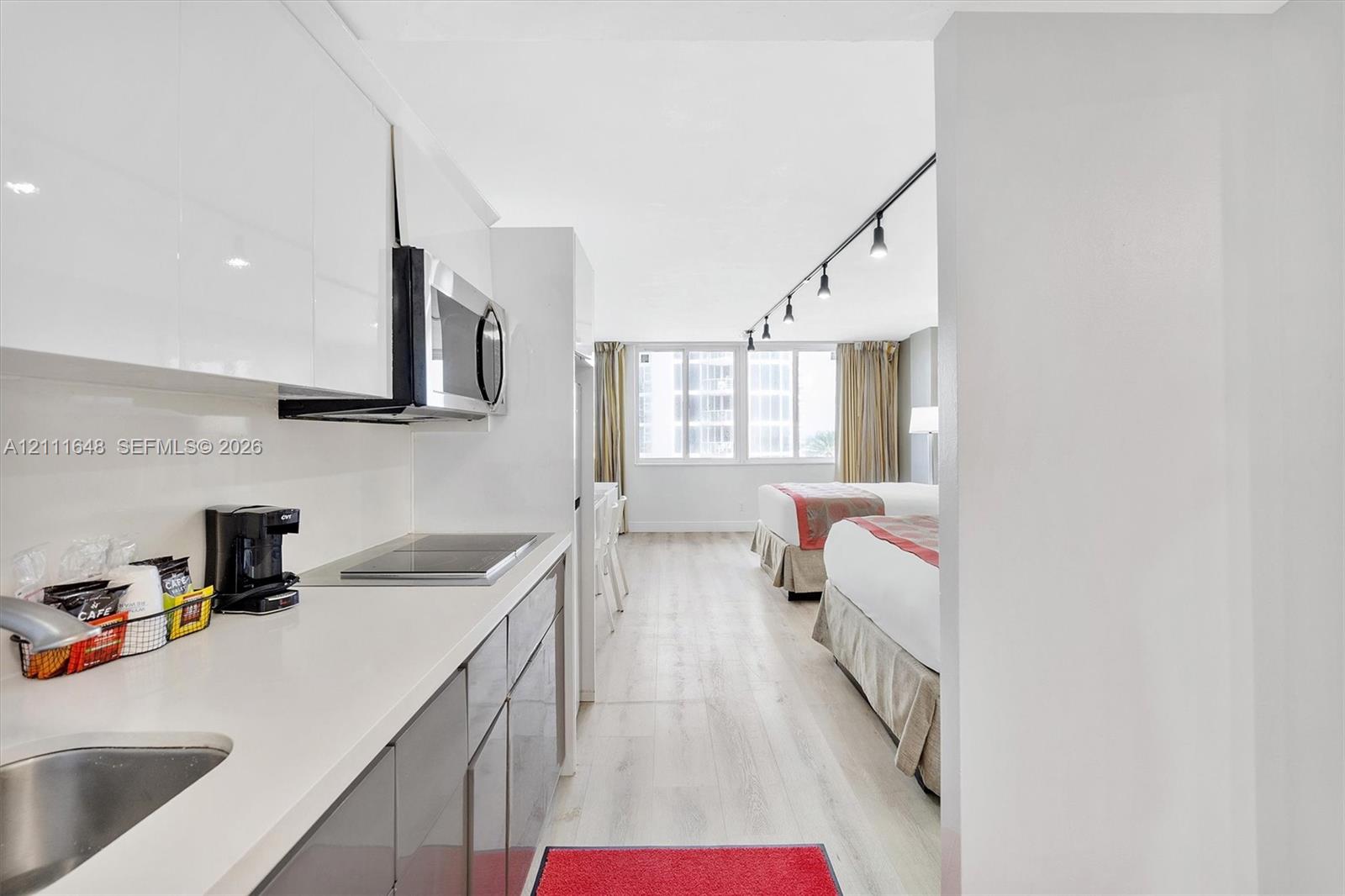 Kitchen featuring high-gloss cabinetry, stone-finish countertops, integrated microwave, and built-in cooktop, complemented by wood-finish flooring and modern track lighting