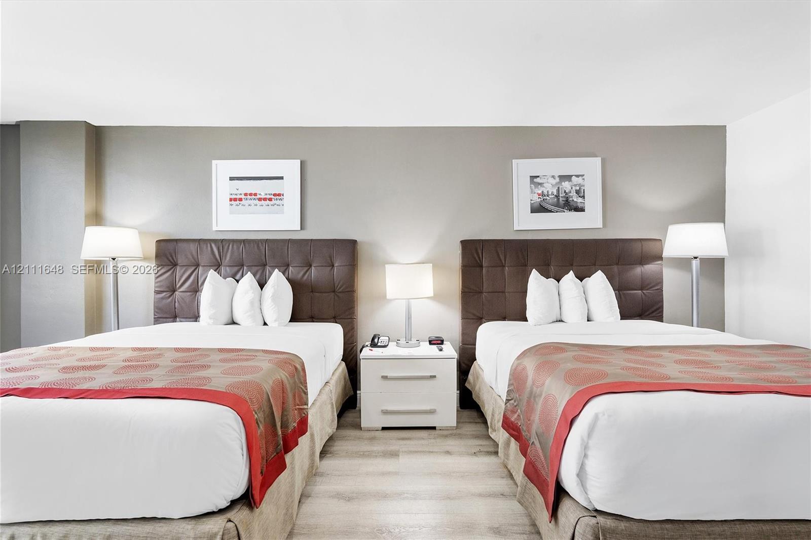 Light-toned wood-finish flooring and a central white two-drawer nightstand with a metallic finish hardware