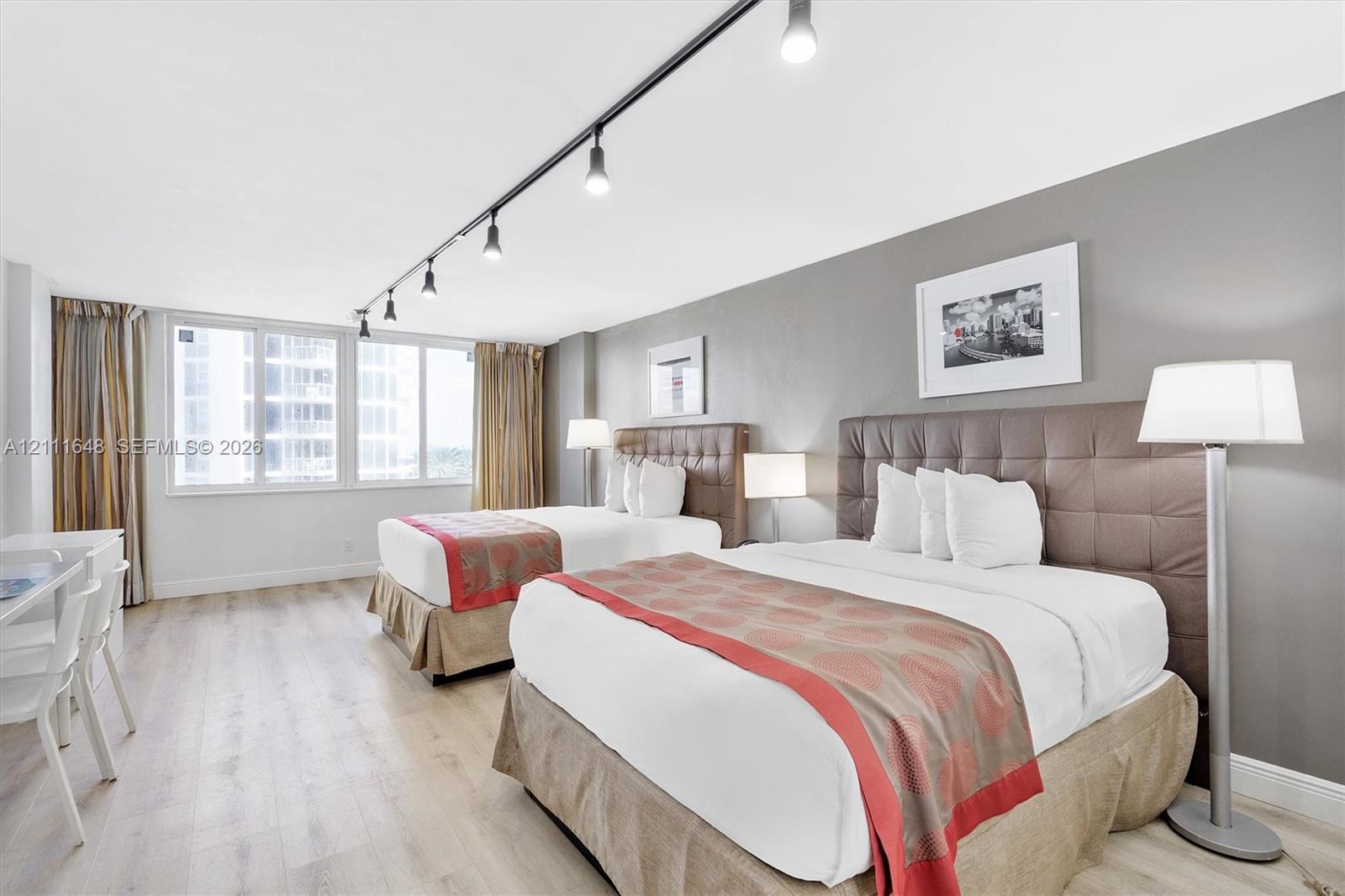 Expansive room featuring wood-finish flooring, neutral gray accent walls, and large windows with integrated track lighting