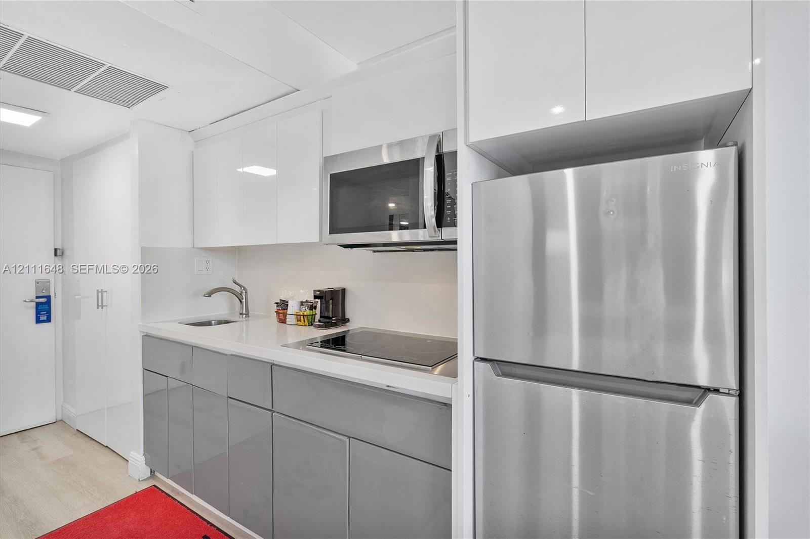 Kitchen featuring high-gloss white upper cabinetry, grey lower cabinetry, stainless steel refrigerator, built-in microwave, and integrated cooktop