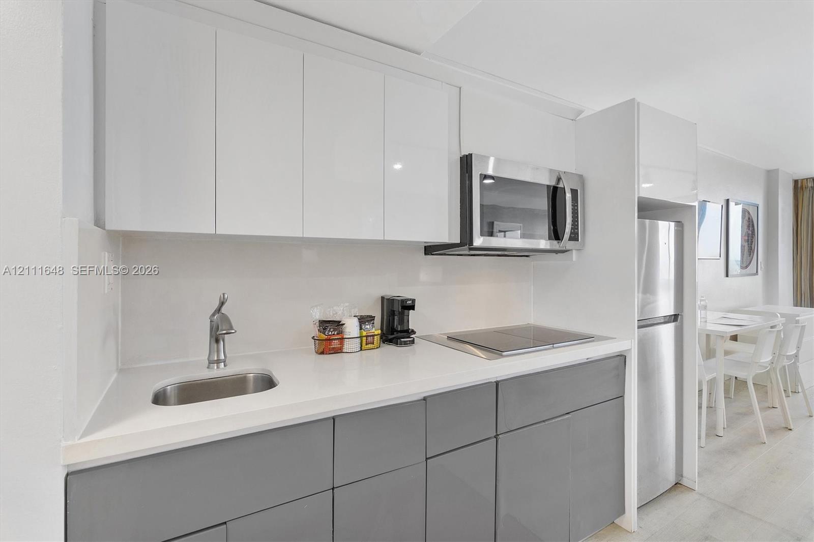 Kitchenette featuring flat-panel white upper cabinets, grey lower cabinetry, stainless steel appliances, solid surface countertops, and an integrated basin sink
