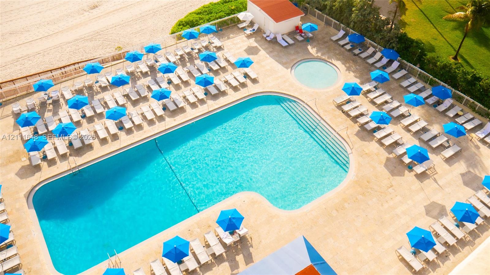 Expansive outdoor pool area featuring stone-paver decking, a secondary circular wading pool, direct beach access, and surrounding landscaped grounds
