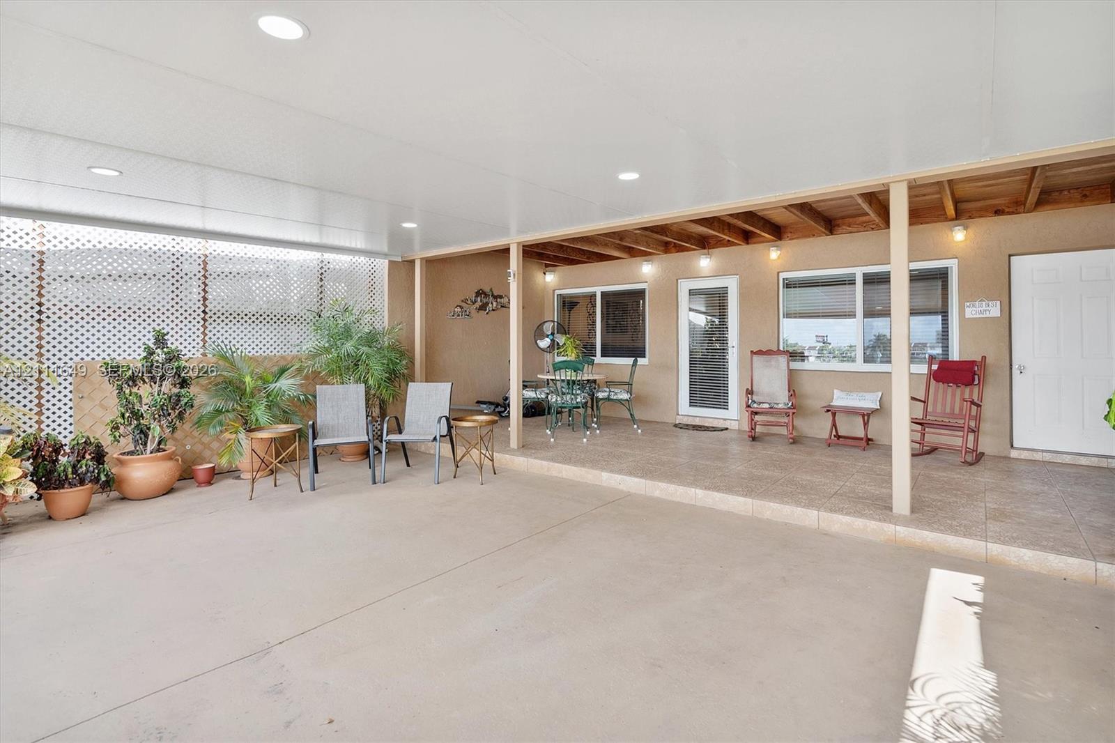 Covered outdoor patio featuring a concrete floor, recessed lighting, exposed wood ceiling beams, and white lattice privacy screening Covered outdoor patio featuring a concrete floor, recessed lighting, exposed wood ceiling beams, and white lattice privacy screening