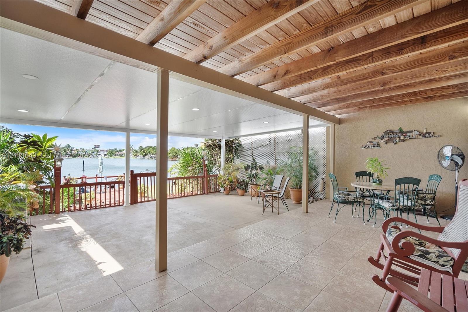 Covered patio featuring a tile floor, exposed wood beam ceiling, recessed lighting, and a railed wood deck overlooking the water Covered patio featuring a tile floor, exposed wood beam ceiling, recessed lighting, and a railed wood deck overlooking the water