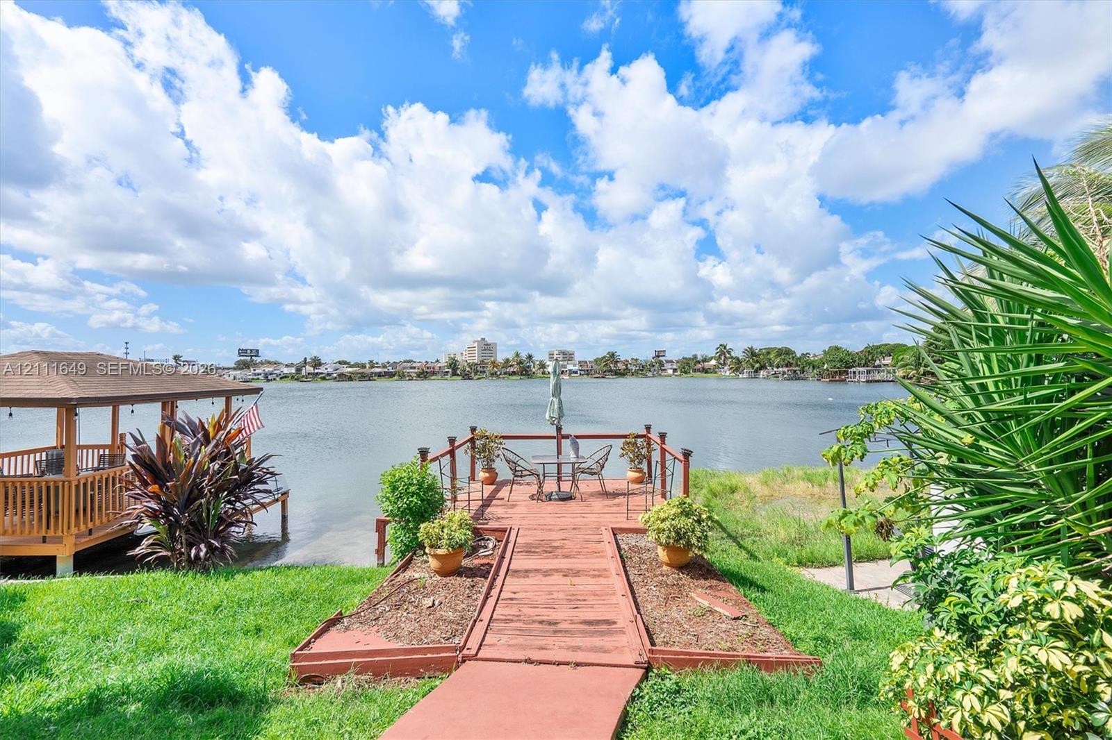 Waterfront property featuring a wooden gazebo, a deck extending over the water, and mature landscaping Waterfront property featuring a wooden gazebo, a deck extending over the water, and mature landscaping