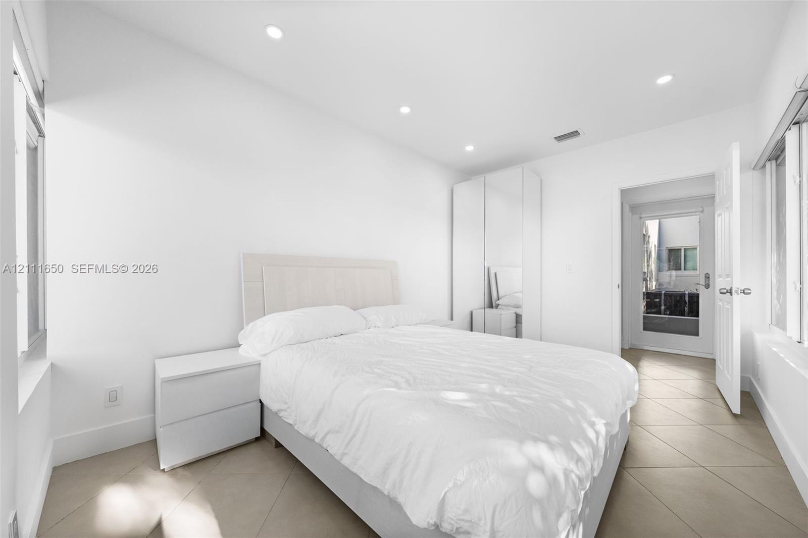 Neutral-toned tile flooring, recessed ceiling lighting, and floor-to-ceiling built-in cabinetry with mirrored panels