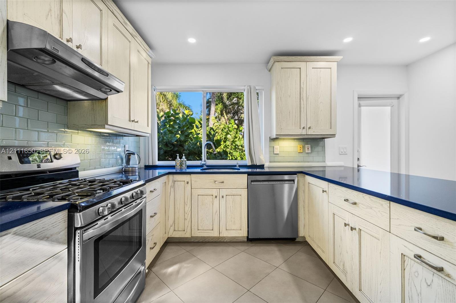Kitchen featuring light-toned wood cabinetry, dark solid-surface countertops, stainless steel appliances, a tile backsplash, and ceramic tile flooring