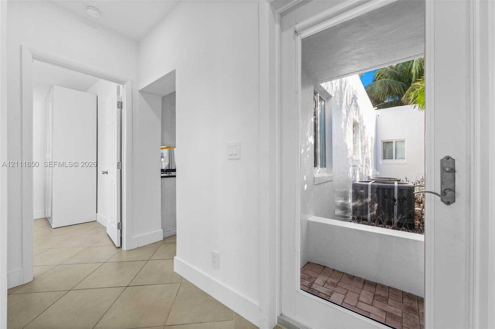 Hallway featuring ceramic tile flooring, solid-core interior doors, and a glass-paneled exterior door opening to a brick-paved patio