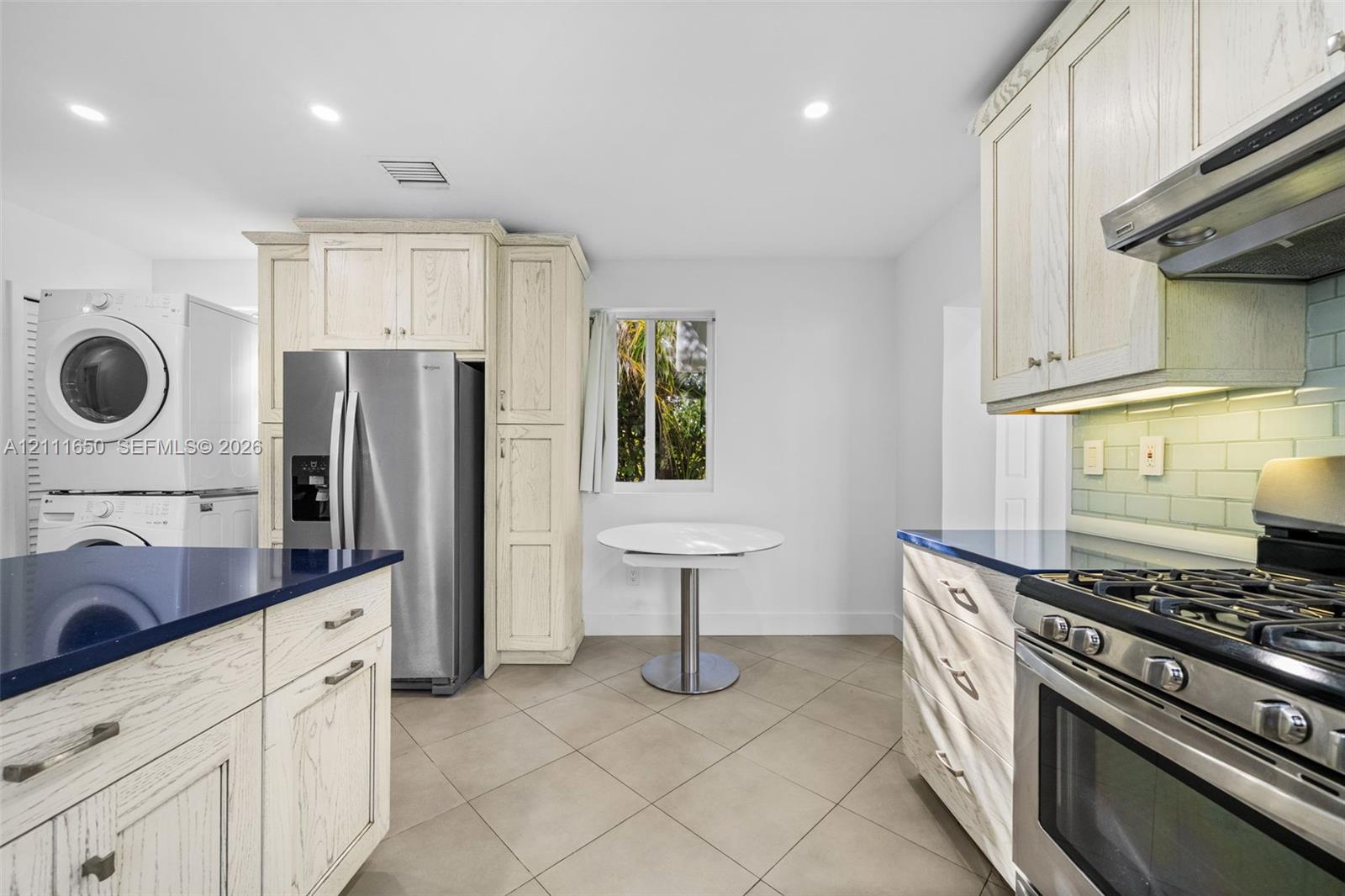 Kitchen featuring light-finish wood cabinetry, dark solid-surface countertops, stainless steel appliances, ceramic tile flooring, and a subway tile backsplash