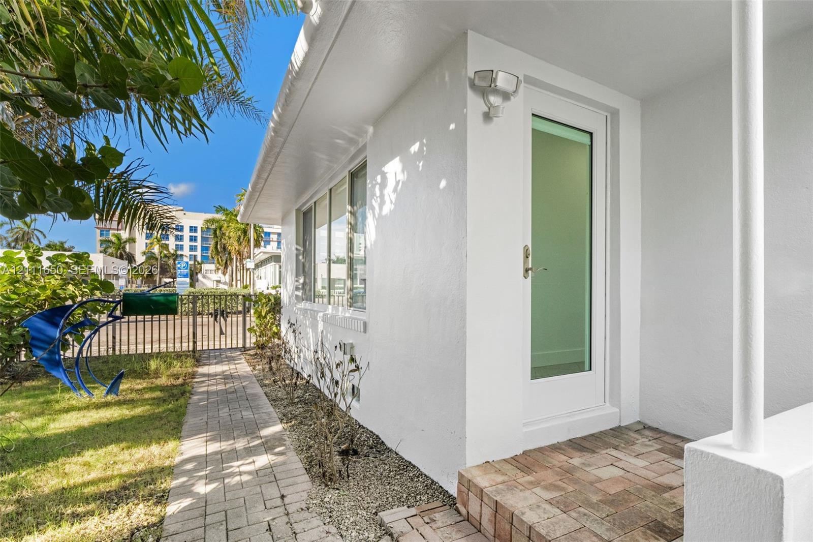 Exterior featuring a white stucco facade, a glass-panel entry door, and a brick paver walkway leading to a brick-paved stoop