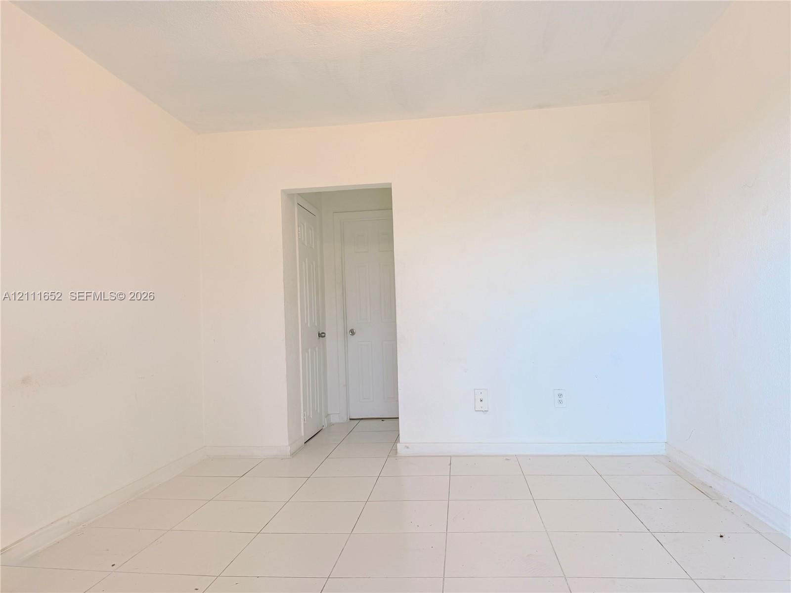 Interior room featuring neutral wall finishes, white tile flooring, and two interior doors with round hardware