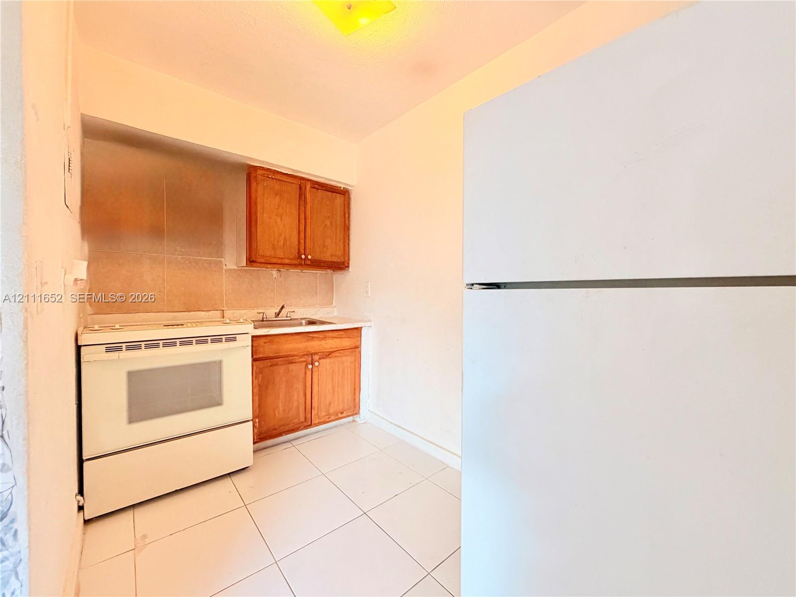 Kitchen area featuring wood cabinetry, white tile flooring, and white stove