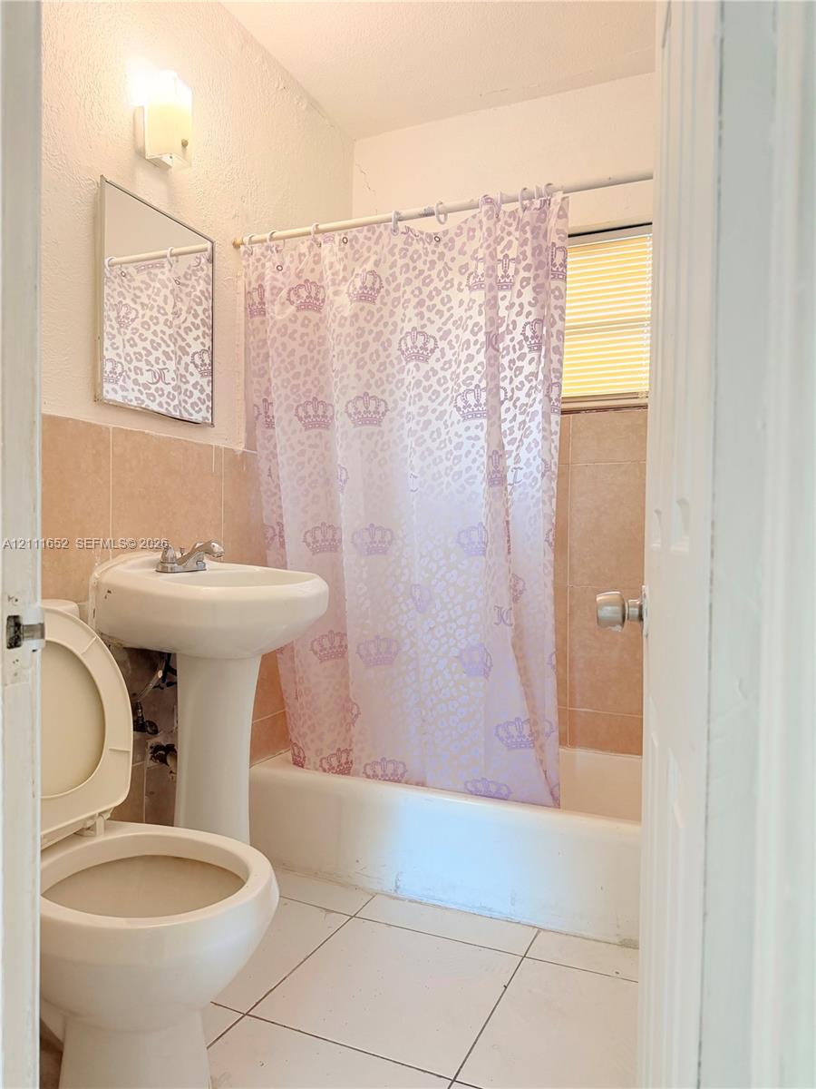 Bathroom featuring a pedestal sink, wall-mounted mirror, light-toned ceramic tile flooring, and a shower-tub combination with ceramic tile surround