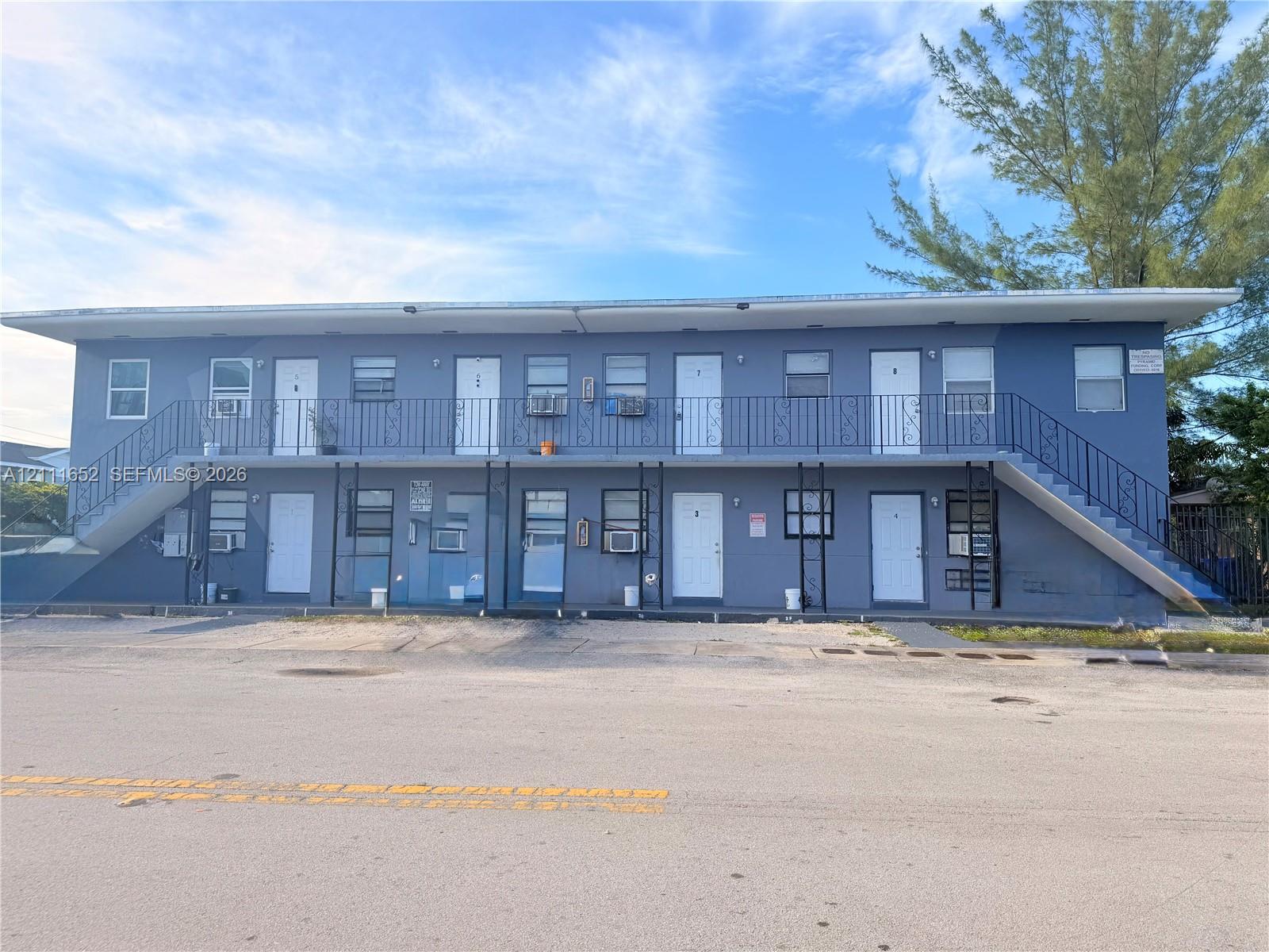 Two-story multi-unit exterior featuring a flat roof, metal railing, and dual exterior staircases