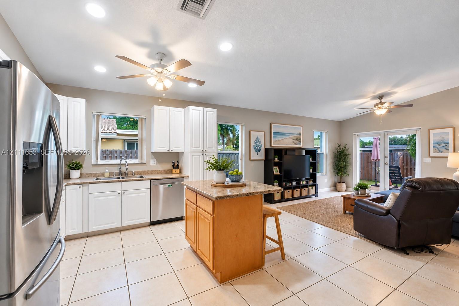 Open-concept kitchen featuring white cabinetry, stone-finish countertops, stainless steel appliances, a center island with wood cabinetry, and neutral-tone tile flooring Open-concept kitchen featuring white cabinetry, stone-finish countertops, stainless steel appliances, a center island with wood cabinetry, and neutral-tone tile flooring