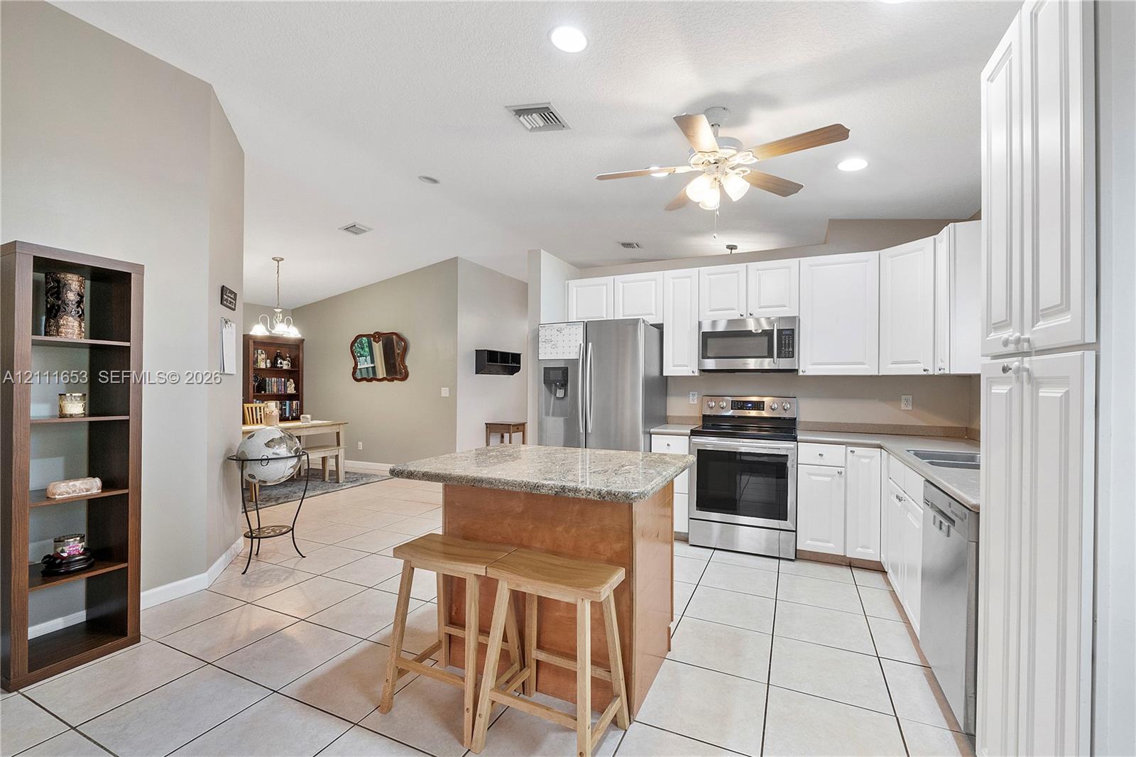 Kitchen featuring white cabinetry, stone-surface countertops, stainless steel appliances, a center island, and tile flooring