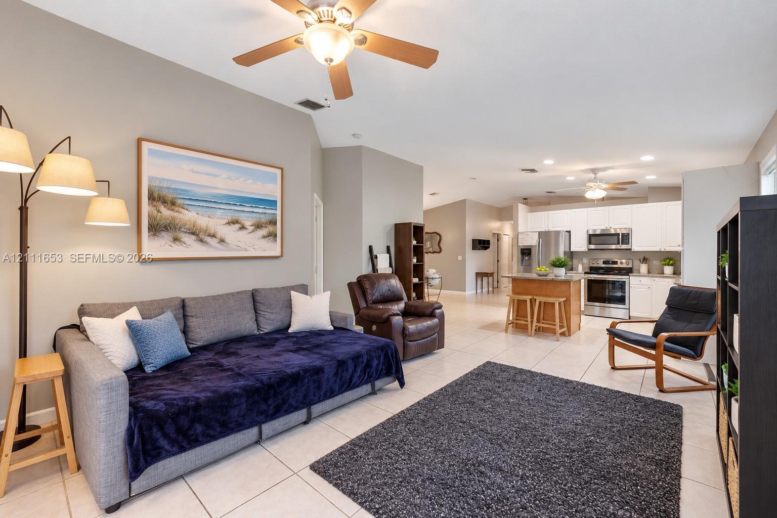 Open-concept interior featuring high vaulted ceilings, light-tone floor tiling, a kitchen island with stone countertops, and recessed lighting Open-concept interior featuring high vaulted ceilings, light-tone floor tiling, a kitchen island with stone countertops, and recessed lighting
