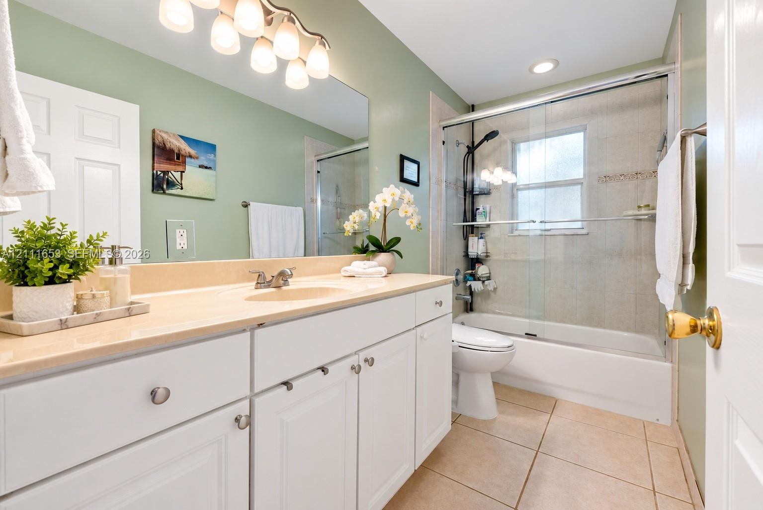 Guest Bathroom featuring white cabinetry, integrated sink, large wall-mounted mirror, ceramic tile flooring, and a shower-tub combination with glass enclosure