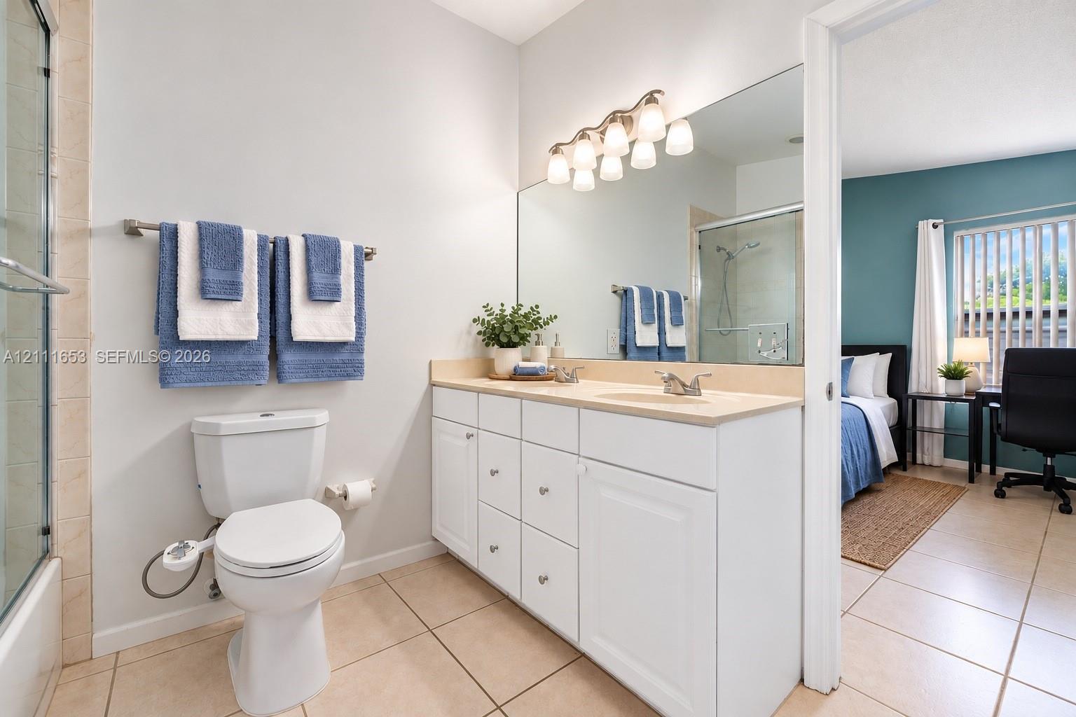 Primary Bathroom featuring white cabinetry, solid-surface vanity countertop with dual integrated sinks, full-width wall mirror, and tile flooring