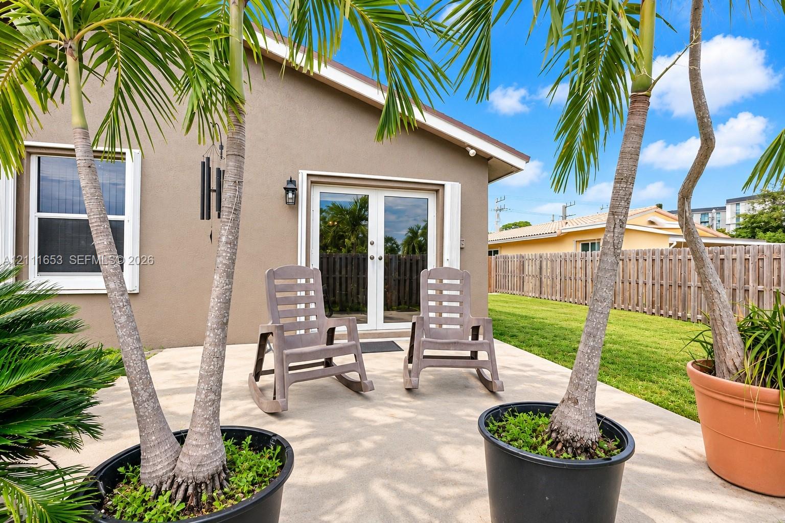 Concrete patio featuring a set of exterior French doors, an attached exterior wall-mounted light fixture, and an adjoining lawn enclosed by a wooden fence