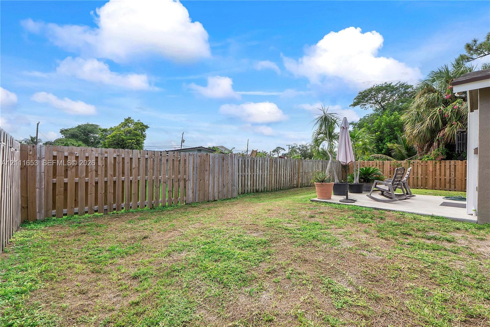 Fenced backyard featuring a concrete patio and open green space
