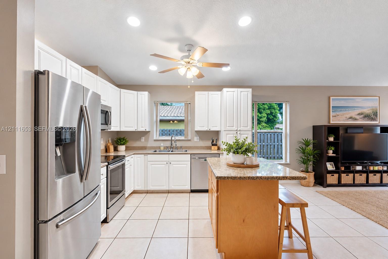Kitchen featuring white shaker-style cabinetry, stone-finish countertops, stainless steel appliances, a center island, and tile flooring