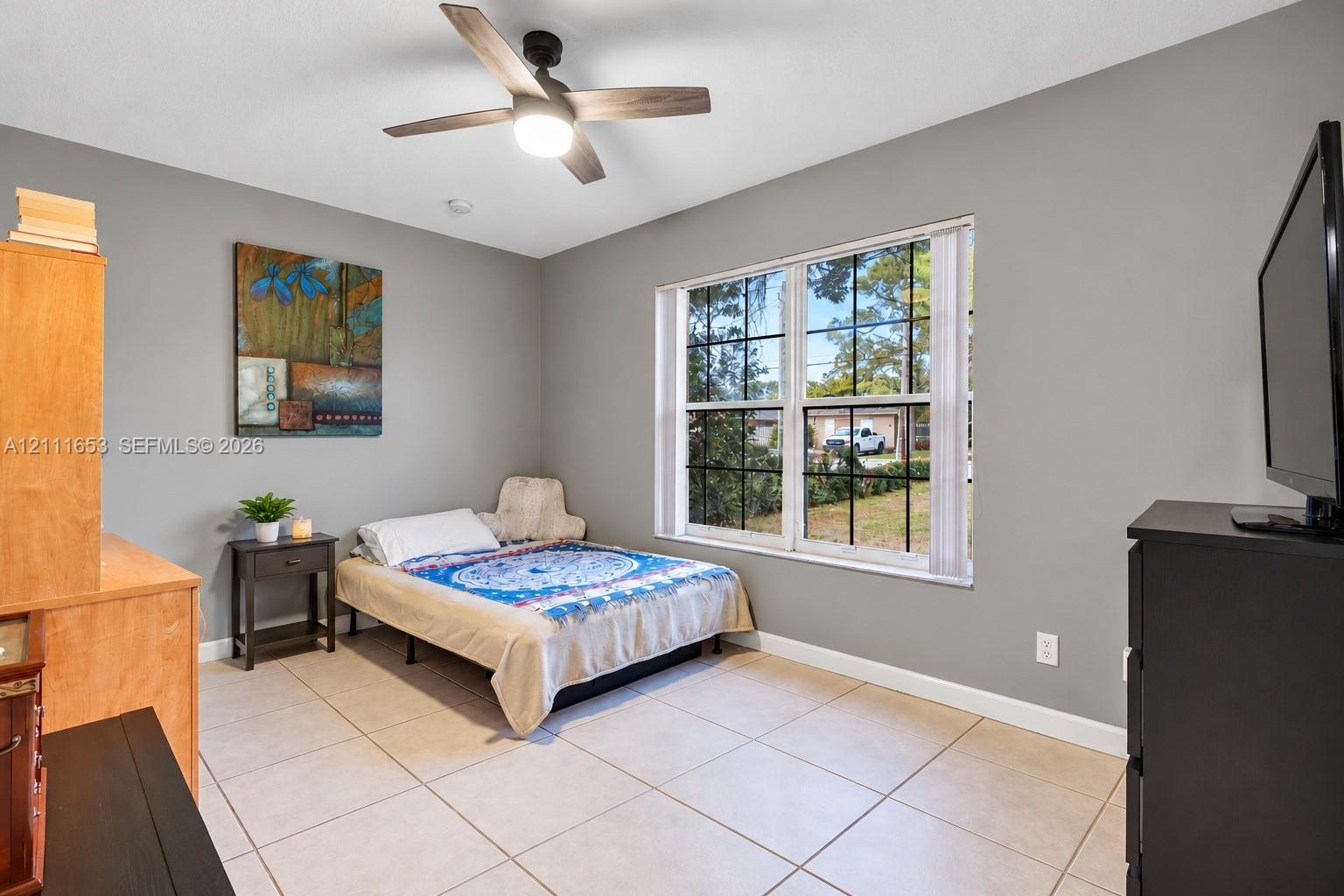 Bedroom 3 Neutral-toned walls featuring large-format ceramic tile flooring, a multi-pane window with grid detailing, and a modern ceiling fan with integrated lighting Bedroom 3 Neutral-toned walls featuring large-format ceramic tile flooring, a multi-pane window with grid detailing, and a modern ceiling fan with integrated lighting