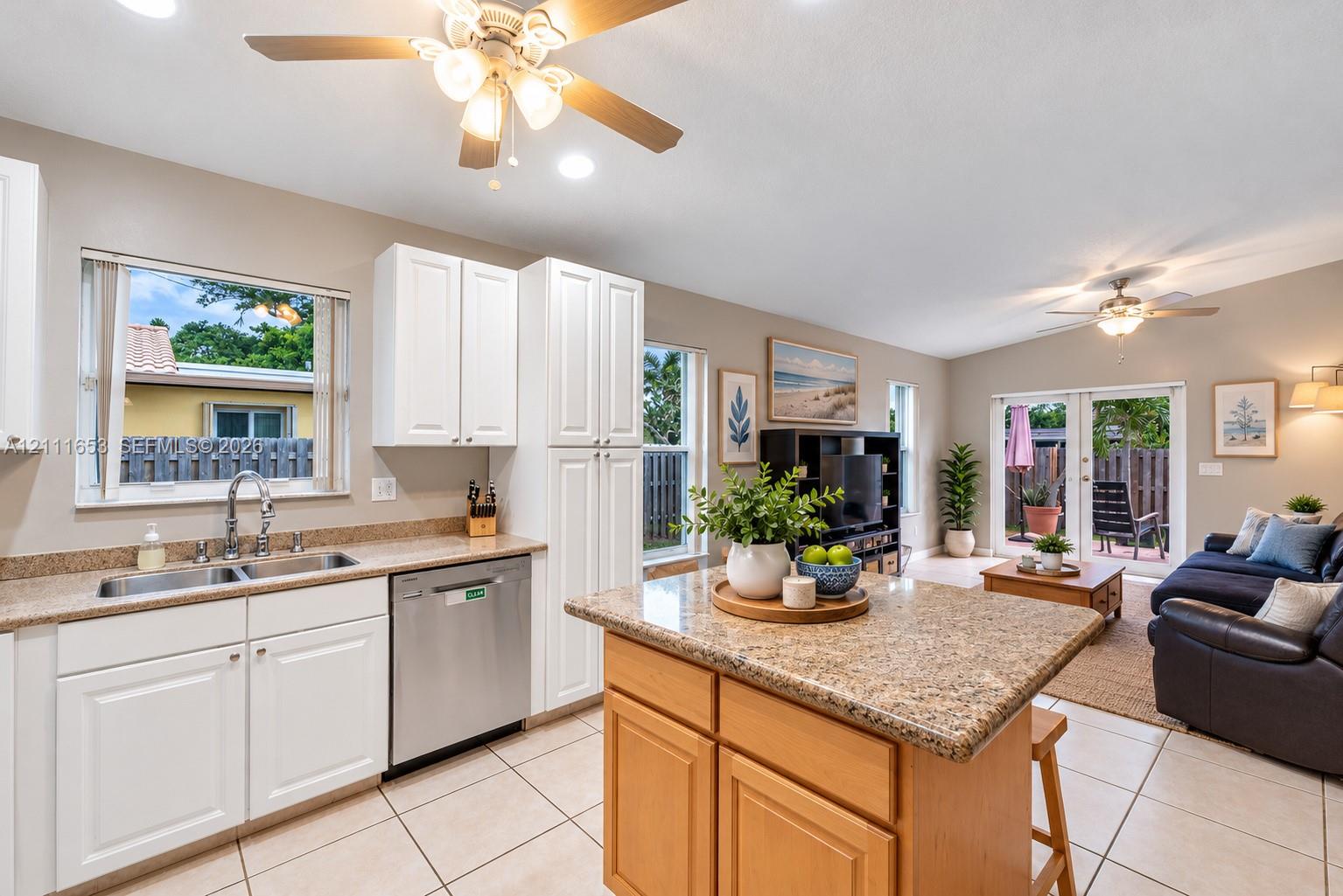 Kitchen featuring white cabinetry, stone-finish countertops, stainless steel dual-basin sink, center island, and neutral tile flooring