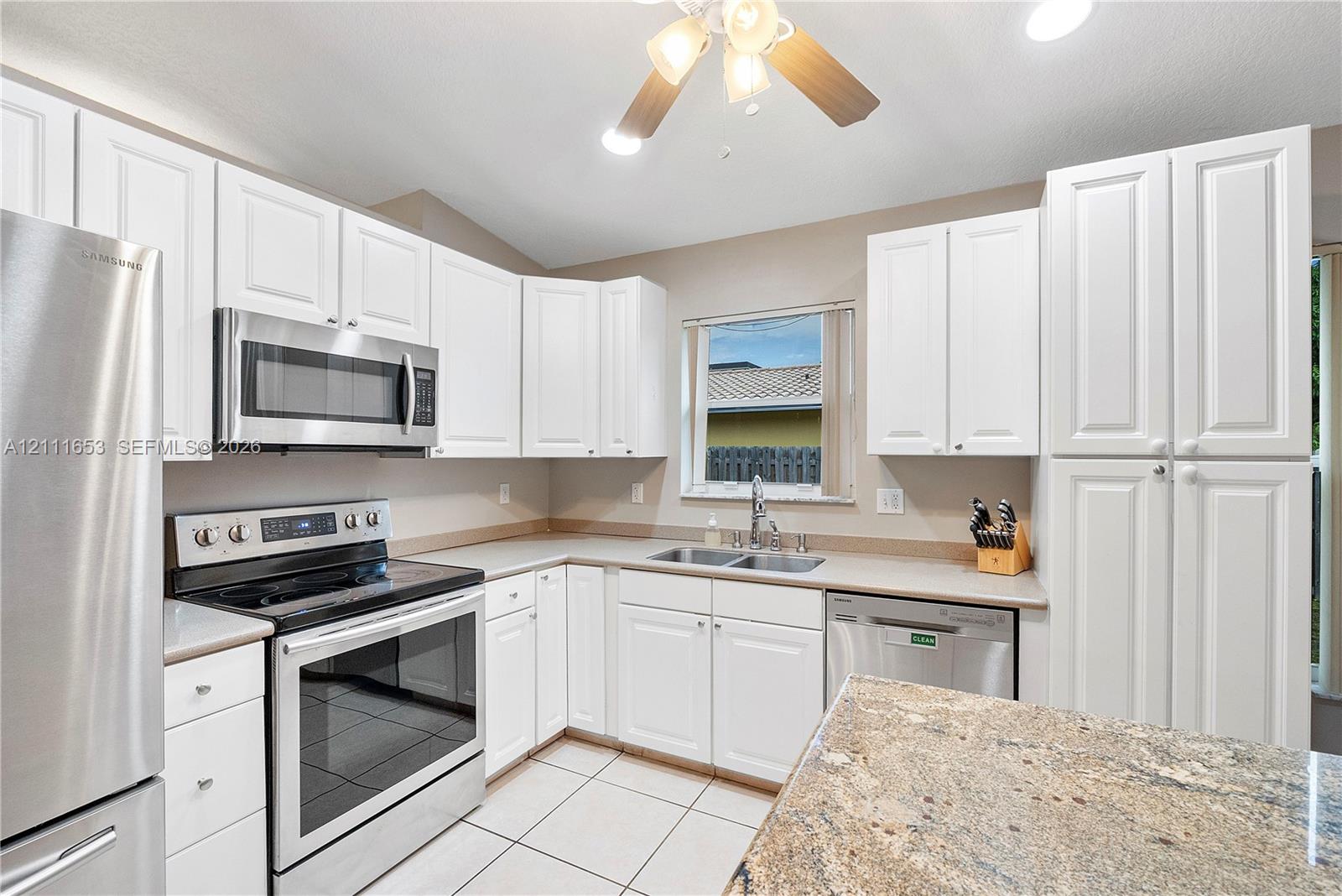 Kitchen featuring white cabinetry, stainless steel appliances, stone-surface countertops, and tile flooring