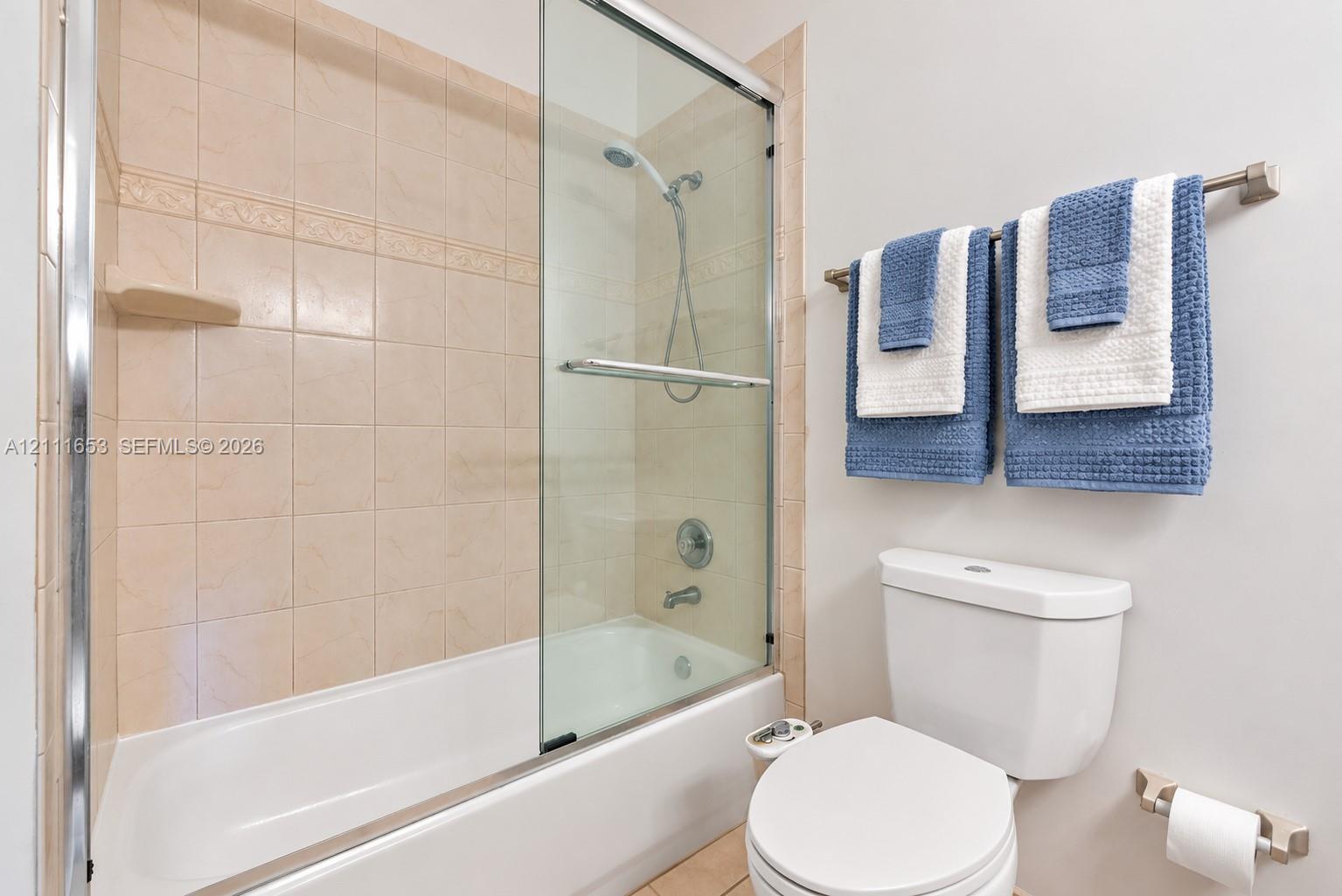 Primary Bath tub and shower combination featuring a glass sliding door, ceramic wall tile surround, and metal hardware