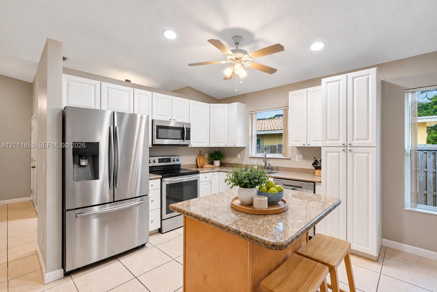 Kitchen featuring white cabinetry, stone-finish countertops, stainless steel appliances, a center island, and ceramic tile flooring Kitchen featuring white cabinetry, stone-finish countertops, stainless steel appliances, a center island, and ceramic tile flooring