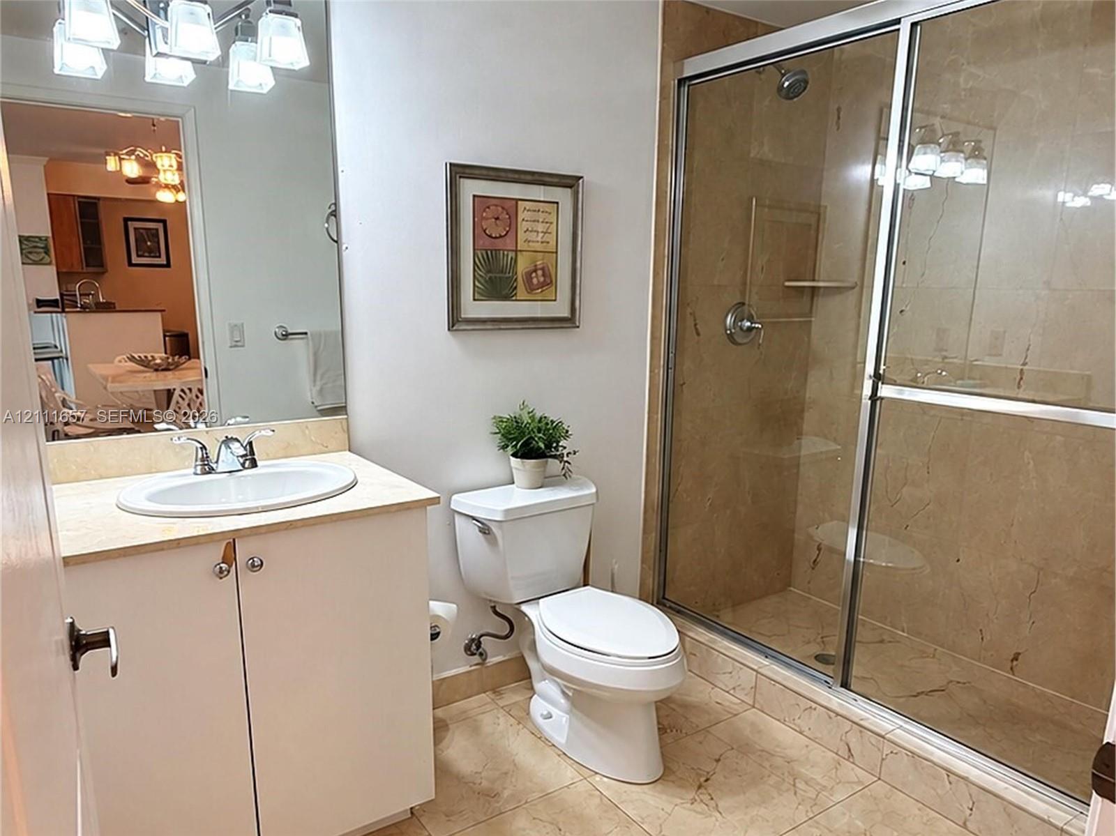Bathroom featuring large-format tile flooring, a shower with a glass sliding enclosure, a vanity with a light-toned countertop, and a multi-light fixture over a wall-mounted mirror