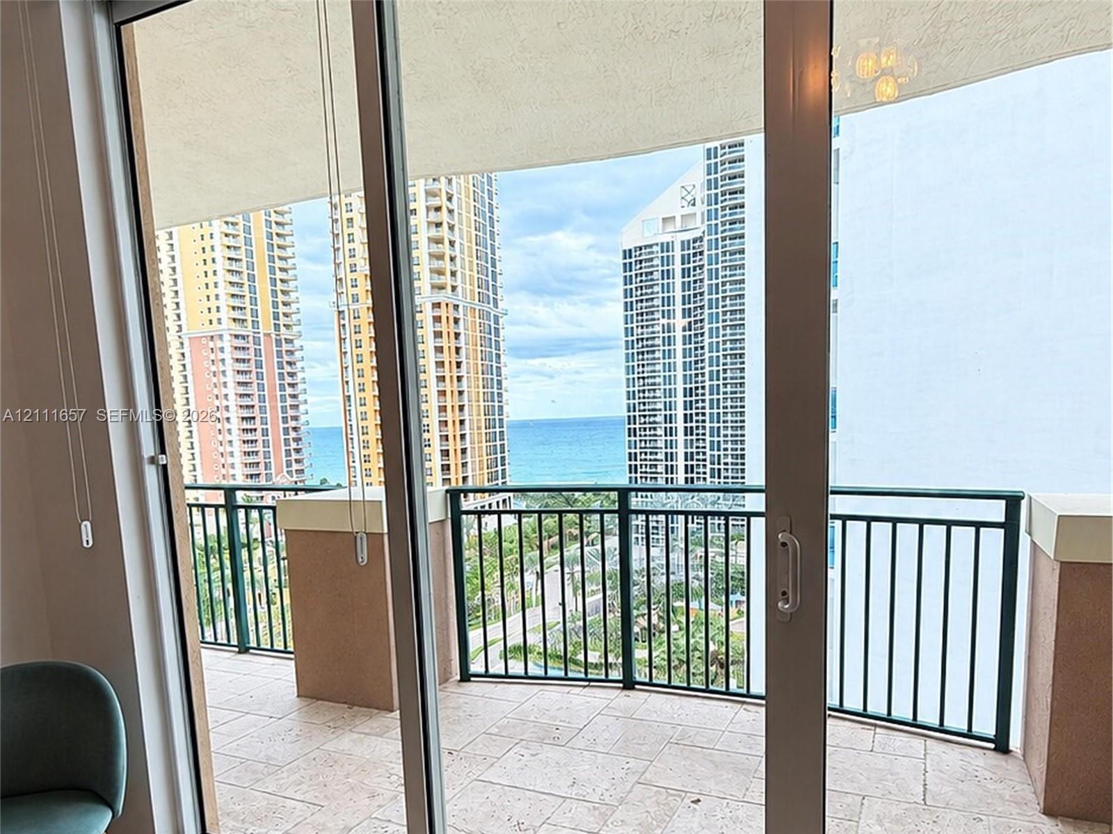 Floor-to-ceiling glass sliding doors opening to a covered terrace featuring natural stone tile flooring and a black metal railing