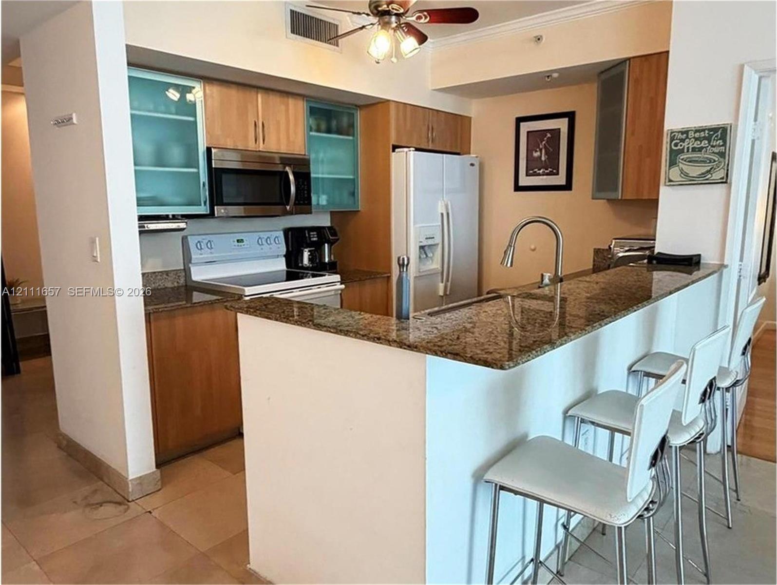 Kitchen featuring natural wood-finish cabinetry with glass-front accents, stone countertops, breakfast bar, and stainless steel microwave