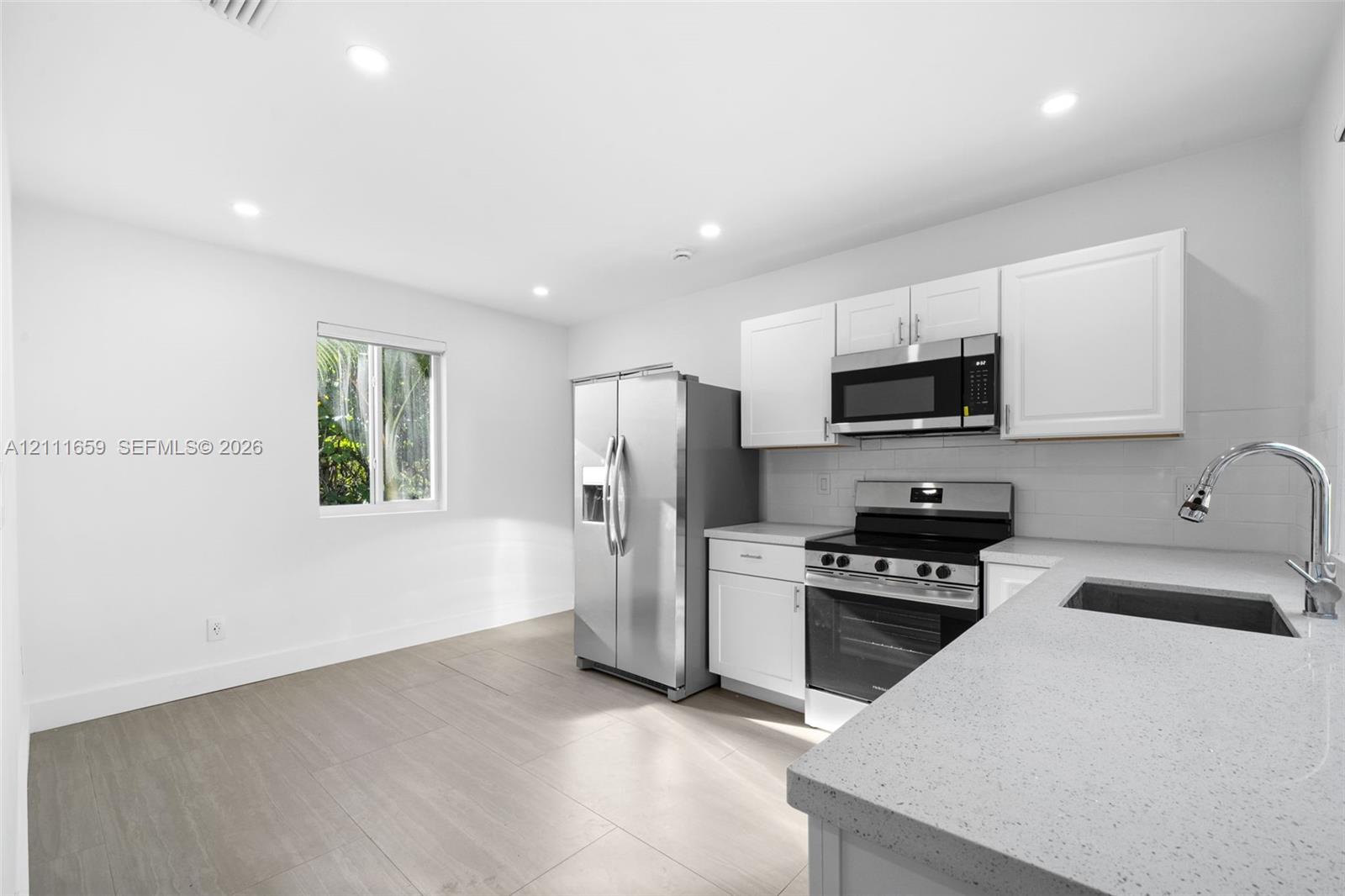 Kitchen featuring white shaker-style cabinetry, solid-surface countertops, recessed lighting, wood-finish flooring, and stainless steel appliances