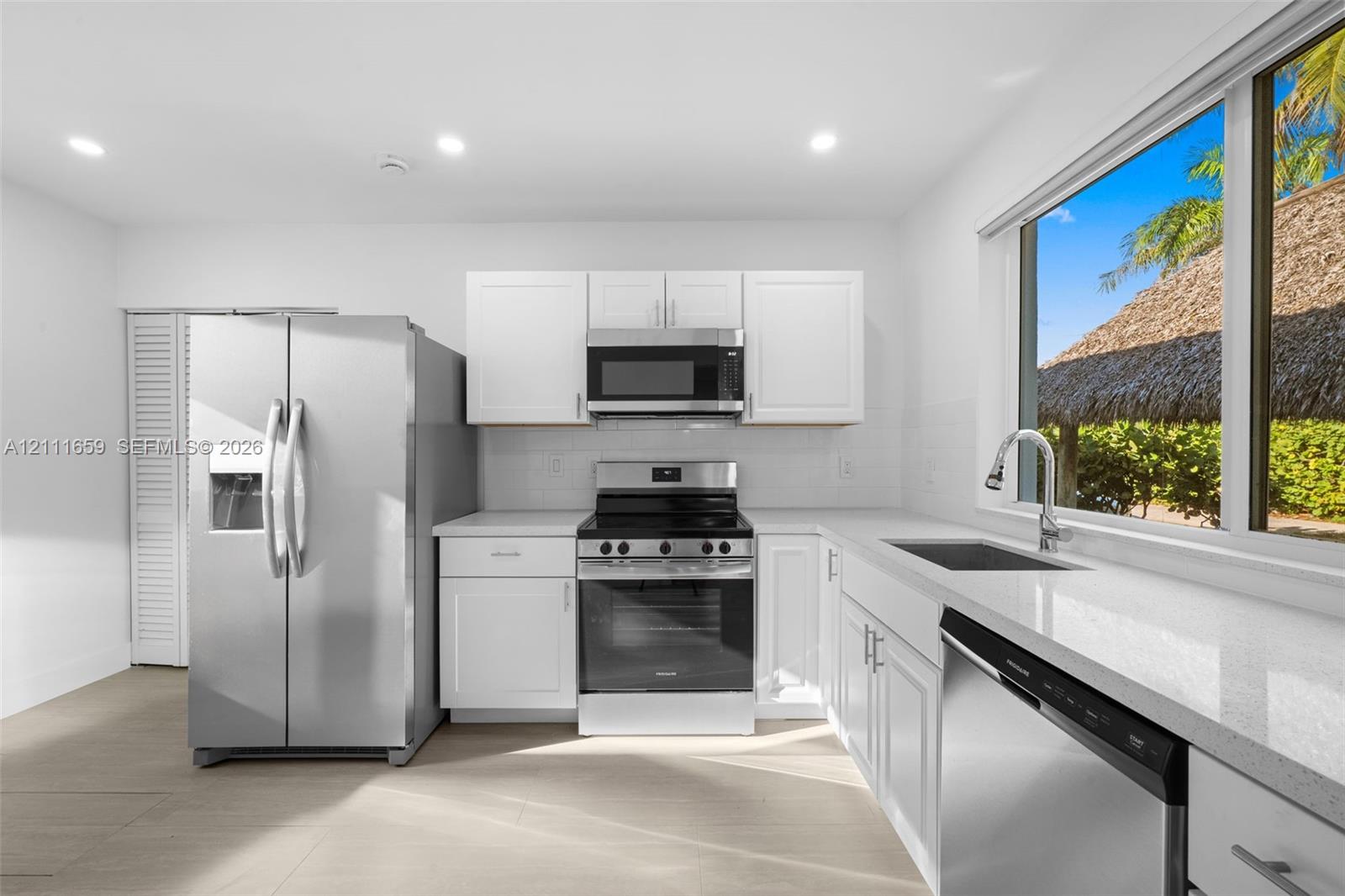 Kitchen featuring white Shaker-style cabinetry, quartz countertops, stainless steel appliances, a single-basin undermount sink with a gooseneck faucet, and tile flooring
