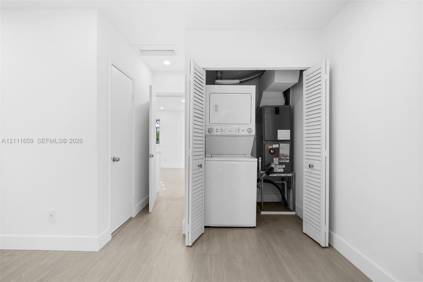 Laundry closet featuring stackable appliances and louvered folding doors, wood-finish flooring, and recessed ceiling lighting