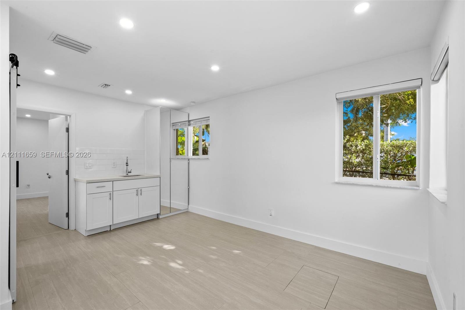 Interior space featuring wood-finish flooring, recessed lighting, white cabinetry with a sink, subway tile backsplash, and mirror-fronted built-in storage
