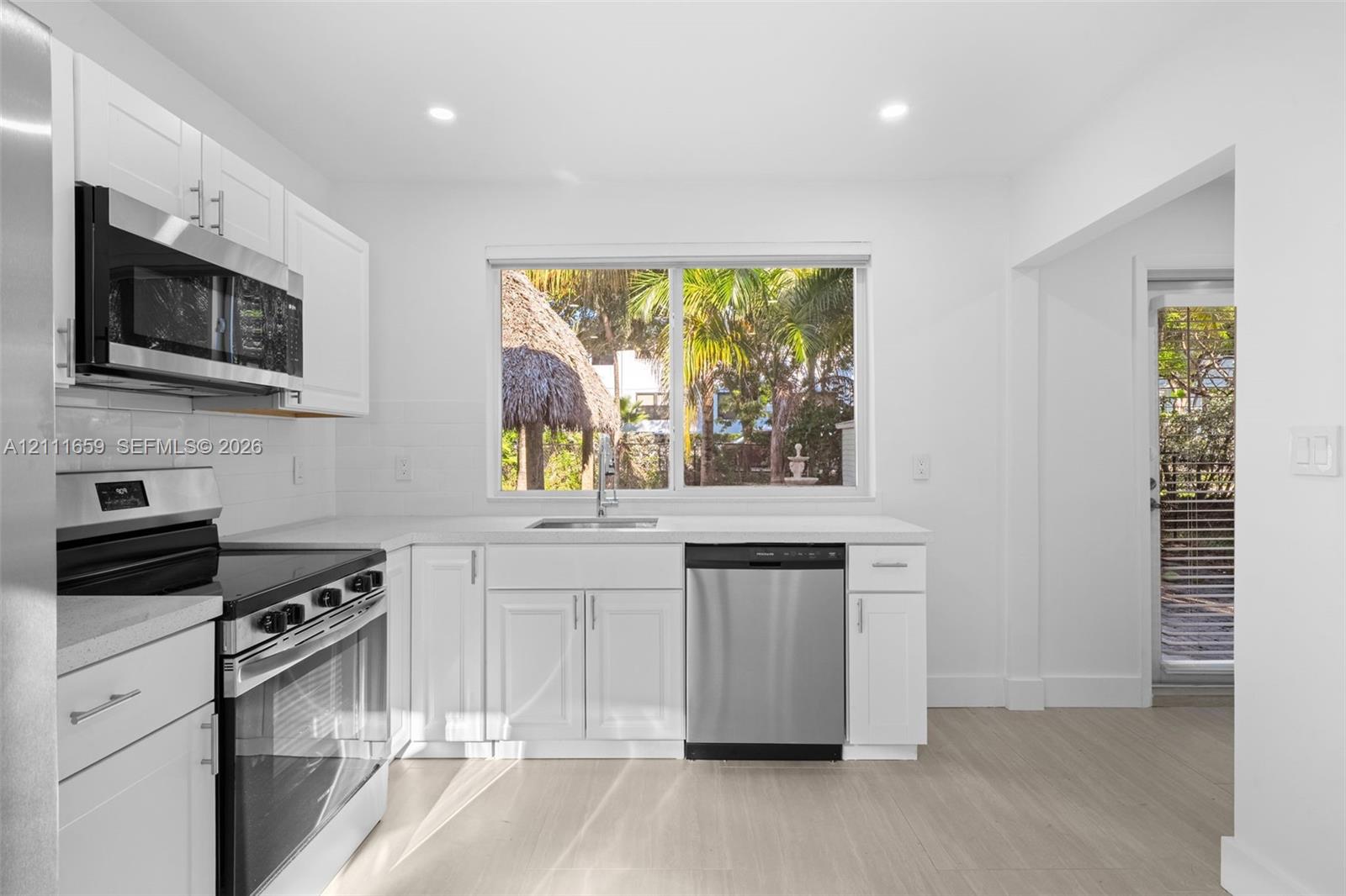 Kitchen featuring white shaker-style cabinetry, stainless steel appliances, solid-surface countertops, recessed lighting, and wood-finish flooring