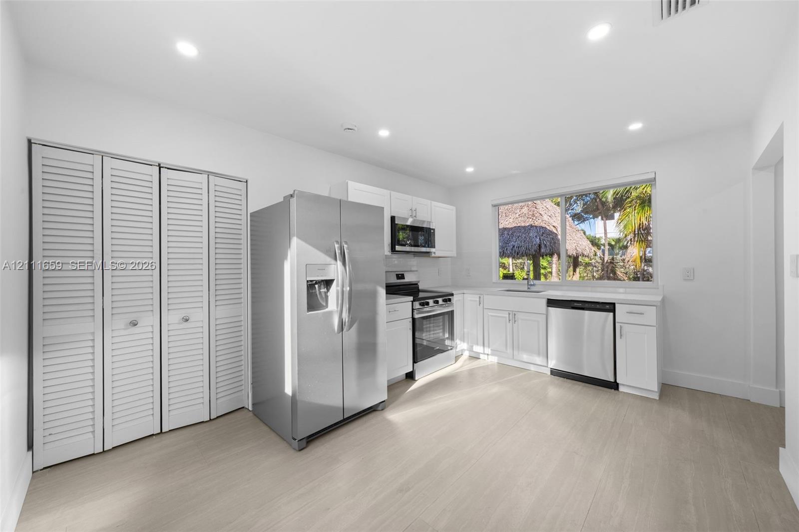 Kitchen featuring white cabinetry, stainless steel appliances, wood-finish flooring, recessed lighting, and louvered closet doors