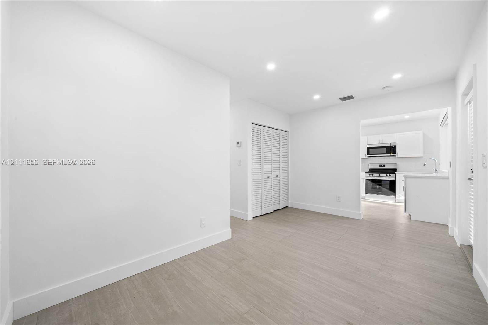 Neutral-toned interior space featuring wood-finish flooring, recessed lighting, white louvered closet doors, and a kitchen equipped with stainless steel appliances
