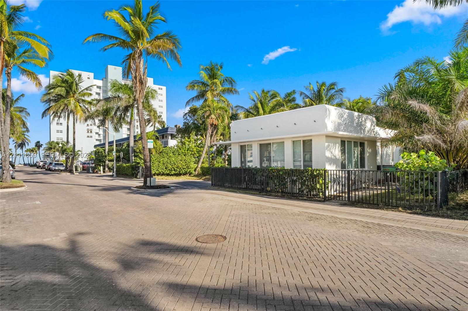 Single-story exterior featuring white stucco finish, flat roofline, metal perimeter fencing, and mature palm landscaping Single-story exterior featuring white stucco finish, flat roofline, metal perimeter fencing, and mature palm landscaping