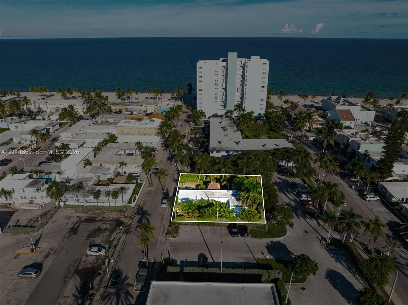 Aerial perspective featuring a flat-roofed structure situated on a corner lot with mature palms and foliage