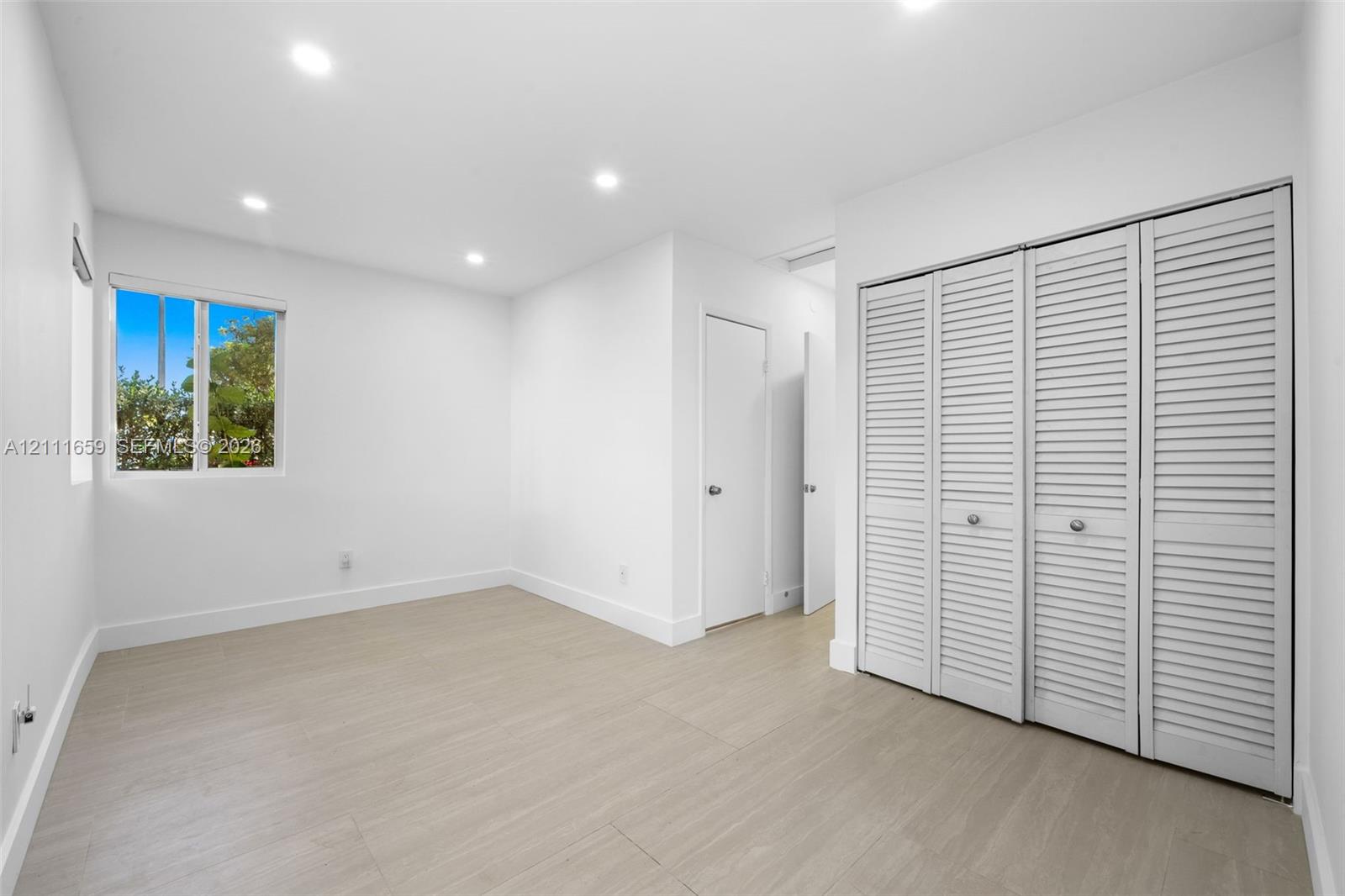 Interior room featuring wood-finish flooring, recessed lighting, white louvered-style bi-fold closet doors, and a single-pane window