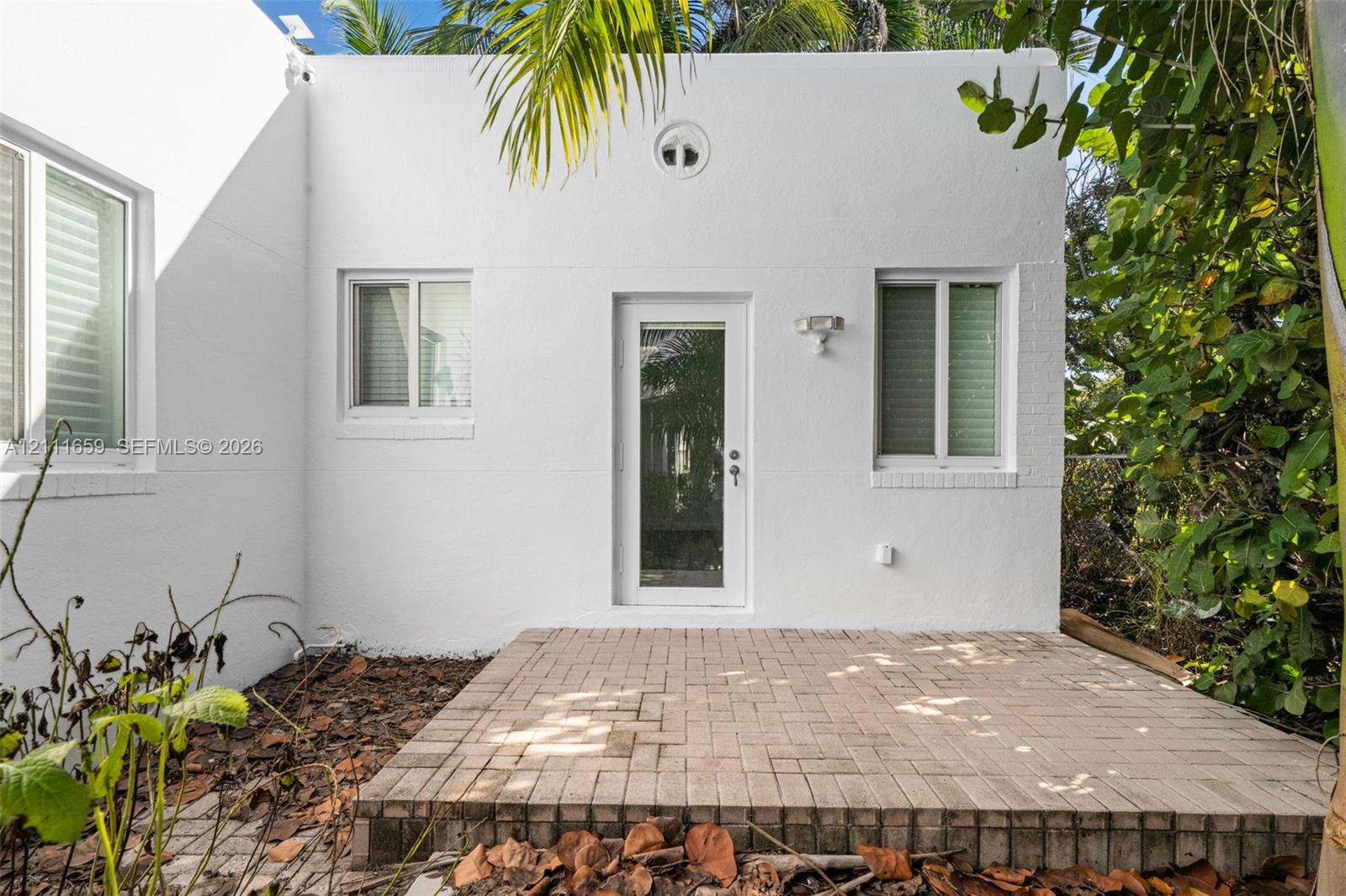 Exterior featuring a white stucco facade, brick paver patio, full-glass panel door, and dual-pane windows