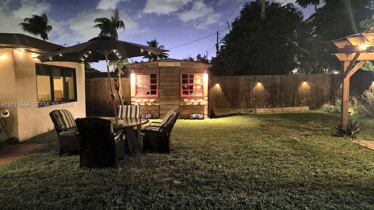 Backyard featuring a wood-sided storage structure, a timber-frame pergola, and perimeter wood fencing with integrated wall-mounted lighting