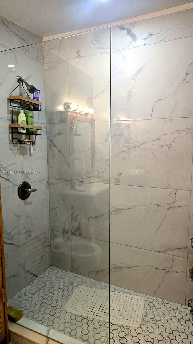 Walk-in shower featuring large-format stone-patterned wall tiles, hexagonal floor tiling, a seamless glass panel, and a wall-mounted shower head